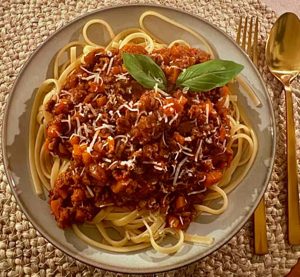 Teller Linguine mit Bolognese, Parmesan und zwei Basilikumblättern in der Draufsicht