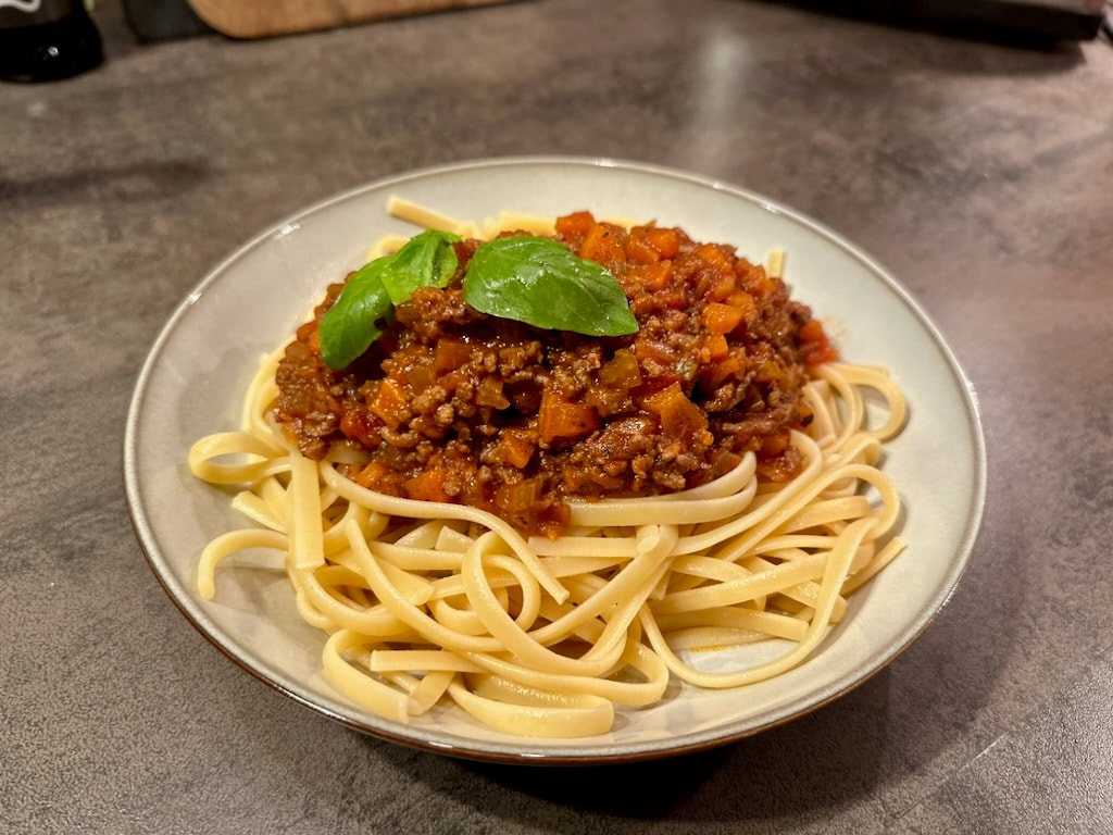 Teller Linguine mit Bolognese und Basilikum auf einer dunklen Arbeitsplatte